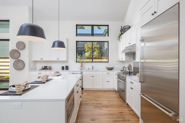 kitchen featuring light hardwood / wood-style floors, built in appliances, hanging light fixtures, light stone countertops, and white cabinets