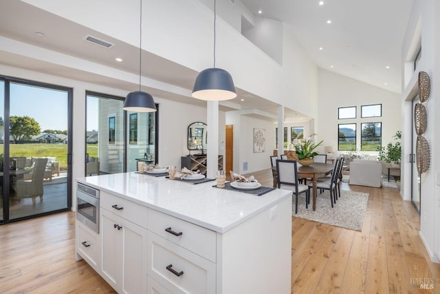 kitchen with light hardwood / wood-style floors, a high ceiling, white cabinetry, hanging light fixtures, and light stone countertops