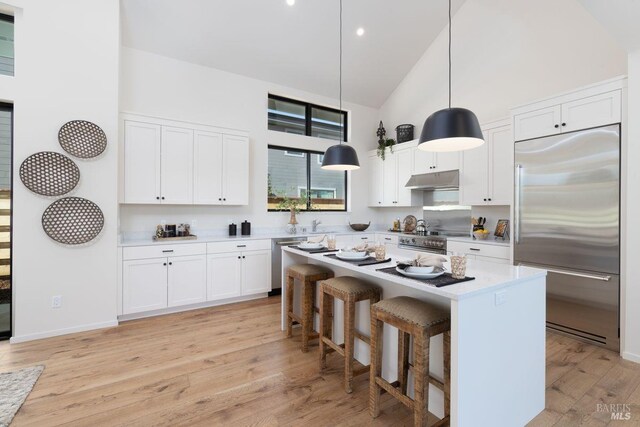 kitchen featuring high vaulted ceiling, high quality appliances, light wood-type flooring, light countertops, and white cabinetry