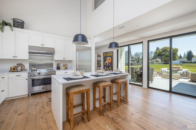 kitchen with decorative light fixtures, a center island, high end stove, white cabinetry, and light wood-type flooring