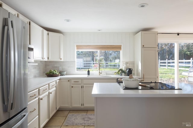 kitchen with white cabinetry, sink, stainless steel fridge, black electric cooktop, and light tile patterned floors