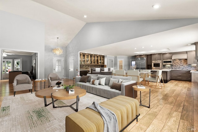 living room with high vaulted ceiling, ceiling fan with notable chandelier, and light hardwood / wood-style floors