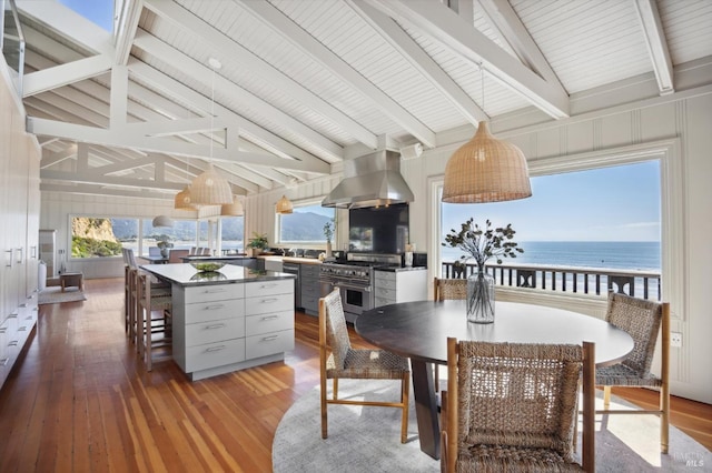 dining room with a view of the beach, vaulted ceiling with beams, a water view, and hardwood / wood-style flooring