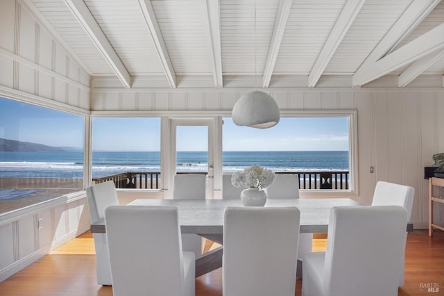 dining area featuring a water view, lofted ceiling with beams, a beach view, and light hardwood / wood-style floors