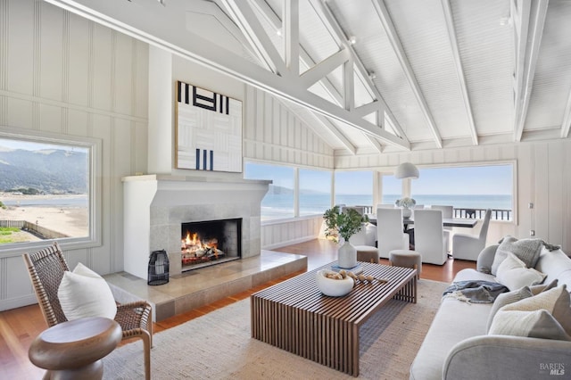 living room featuring beam ceiling, a fireplace, a water view, and light hardwood / wood-style floors