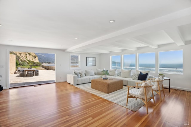 living room with beamed ceiling, a water view, and light hardwood / wood-style flooring