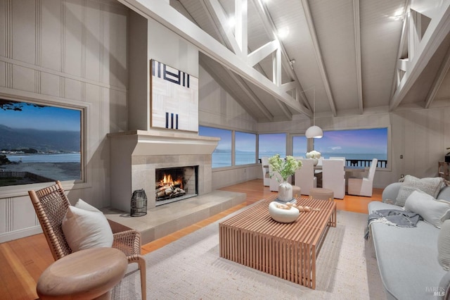 living room with a tile fireplace, beamed ceiling, high vaulted ceiling, hardwood / wood-style floors, and a water view