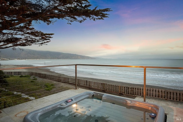 patio terrace at dusk with a water view and a hot tub