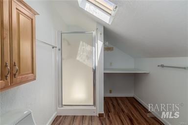 bathroom featuring toilet, vaulted ceiling with skylight, a shower with shower door, and hardwood / wood-style flooring