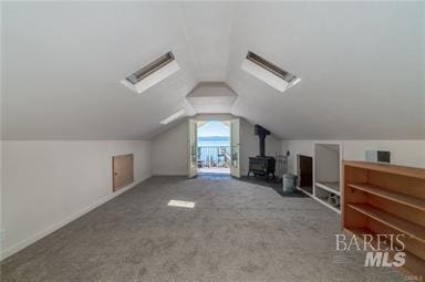 additional living space with carpet flooring, a wood stove, and vaulted ceiling with skylight