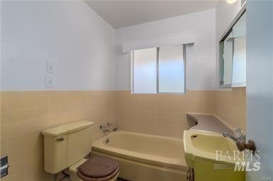 bathroom featuring vanity, toilet, tile walls, and a bathing tub