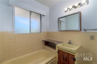 bathroom featuring vanity, a bathtub, and tile walls