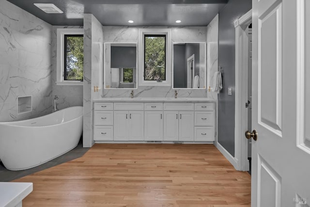 bathroom with hardwood / wood-style flooring, vanity, a bath, and tile walls