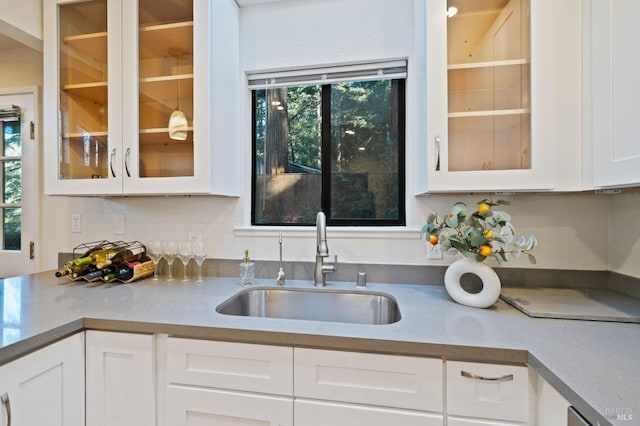 kitchen with white cabinets, light countertops, glass insert cabinets, and a sink