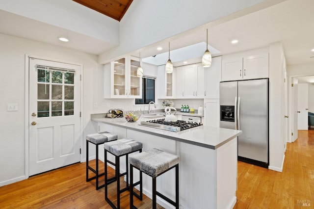 kitchen featuring white cabinetry, a sink, glass insert cabinets, appliances with stainless steel finishes, and a kitchen bar