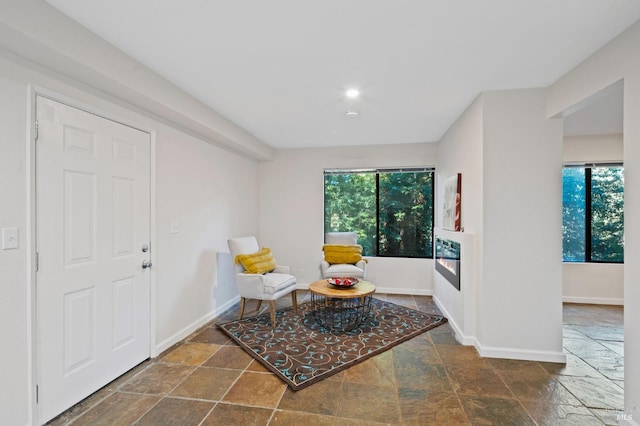 sitting room with a glass covered fireplace, baseboards, and stone tile flooring