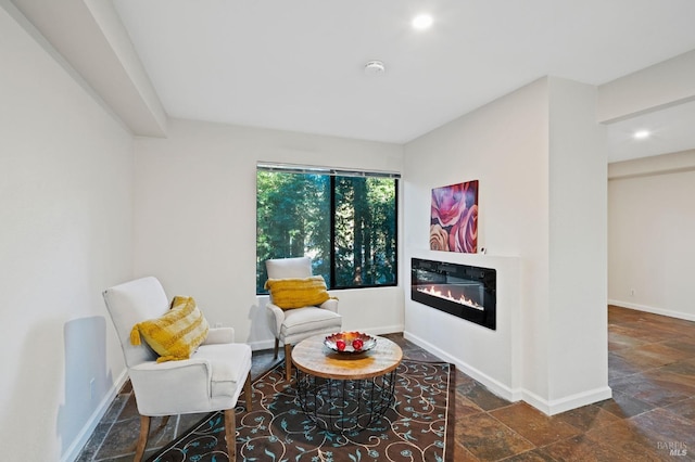living area featuring a glass covered fireplace, recessed lighting, baseboards, and stone tile flooring