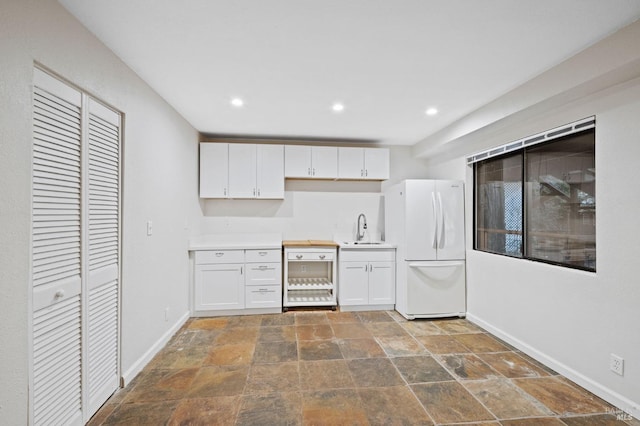 kitchen with baseboards, light countertops, freestanding refrigerator, white cabinetry, and a sink