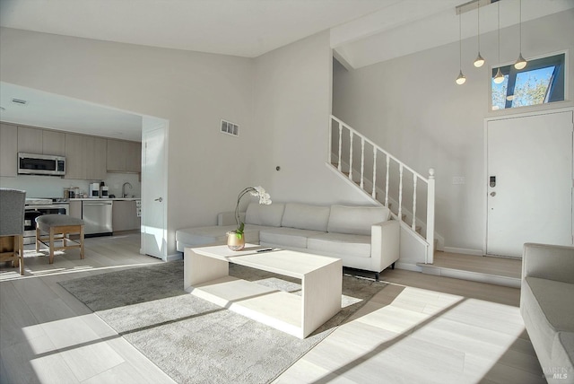 living room featuring light hardwood / wood-style floors, sink, and high vaulted ceiling