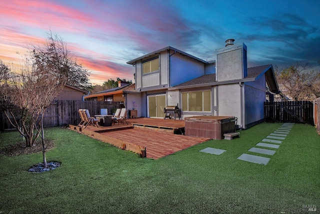 back house at dusk with a lawn, a deck, and a hot tub