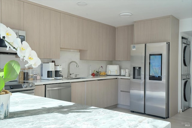 kitchen with light brown cabinetry, sink, stacked washing maching and dryer, and appliances with stainless steel finishes