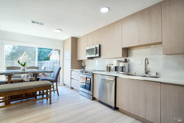 kitchen featuring appliances with stainless steel finishes, light hardwood / wood-style floors, light brown cabinetry, and sink