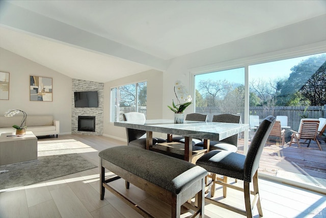 dining area featuring vaulted ceiling with beams, a fireplace, plenty of natural light, and light wood-type flooring