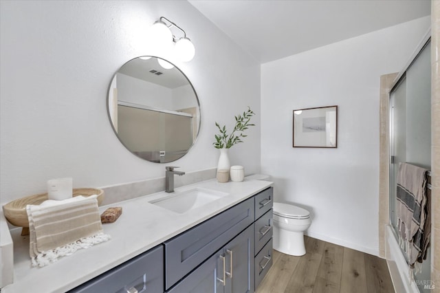 full bathroom featuring vanity, hardwood / wood-style flooring, enclosed tub / shower combo, and toilet