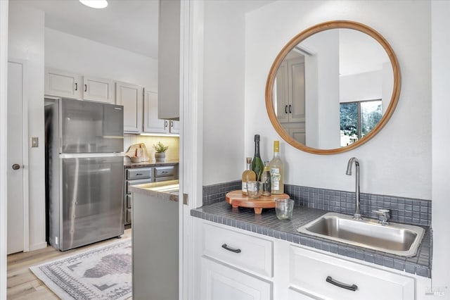 kitchen with stainless steel refrigerator, light hardwood / wood-style floors, sink, and tasteful backsplash