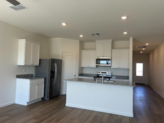 kitchen featuring white cabinets, stainless steel appliances, dark stone counters, and an island with sink