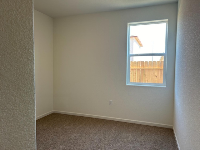 empty room featuring carpet, a textured wall, and baseboards