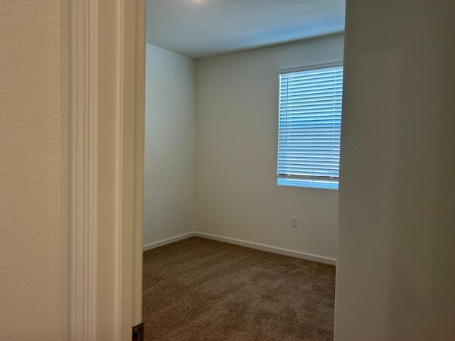 empty room featuring dark colored carpet and baseboards