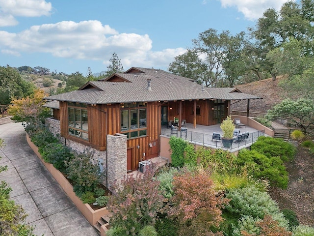 view of front of house featuring stone siding, a patio area, and roof with shingles