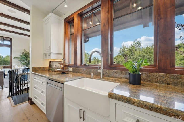 kitchen with stainless steel dishwasher, light wood-style floors, white cabinetry, a sink, and dark stone countertops