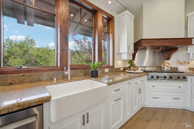 kitchen featuring light wood finished floors, white cabinets, appliances with stainless steel finishes, light countertops, and a sink