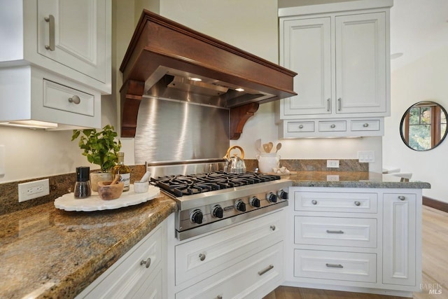 kitchen with light wood-style flooring, white cabinetry, custom exhaust hood, dark stone counters, and stainless steel gas stovetop