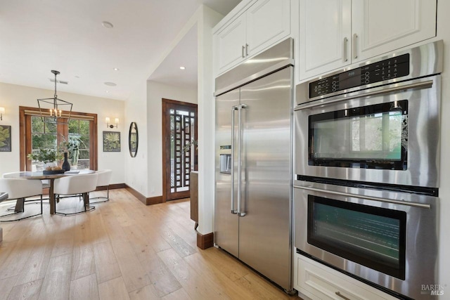 kitchen with stainless steel appliances, baseboards, white cabinets, hanging light fixtures, and light wood finished floors