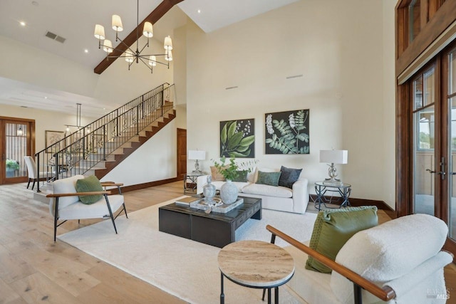 living area with visible vents, a towering ceiling, an inviting chandelier, light wood-type flooring, and stairs