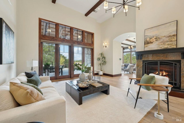 living area with wood finished floors, beamed ceiling, a glass covered fireplace, and a towering ceiling