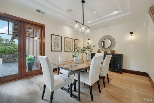 dining area with baseboards, visible vents, a tray ceiling, french doors, and light wood-style floors