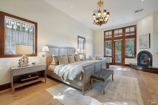 bedroom with a towering ceiling, light wood-style flooring, a glass covered fireplace, and visible vents