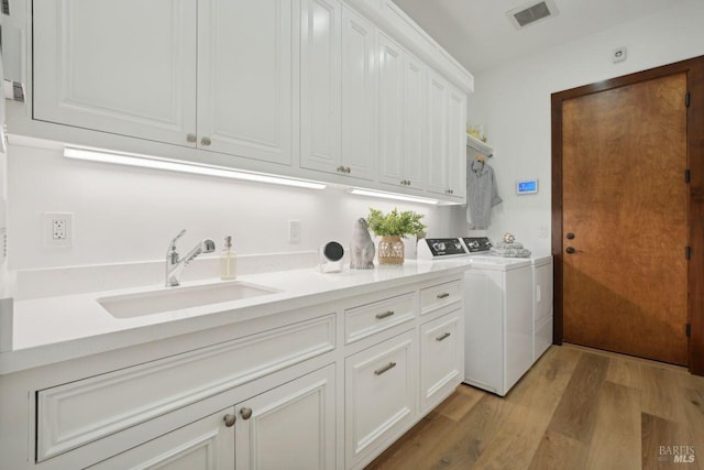 washroom featuring light wood-style flooring, separate washer and dryer, a sink, visible vents, and cabinet space