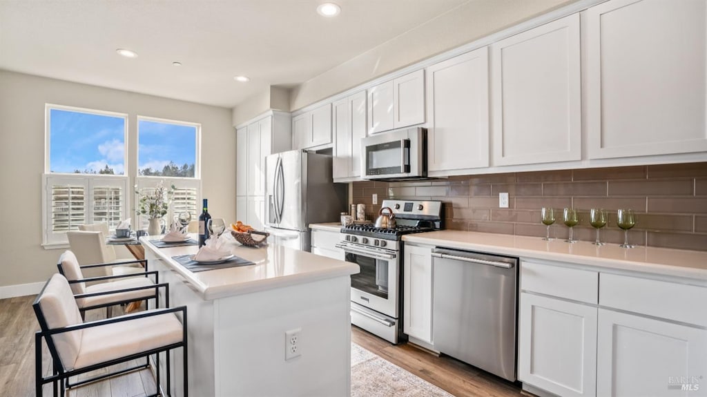 kitchen with a center island, backsplash, appliances with stainless steel finishes, white cabinetry, and a breakfast bar area