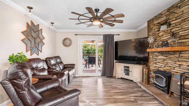 living room featuring hardwood / wood-style flooring, ceiling fan, crown molding, and a wood stove