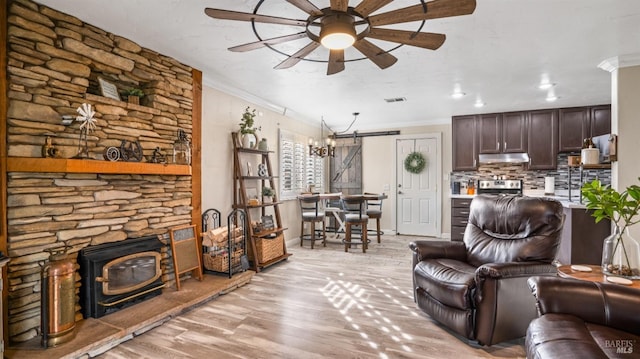 living room featuring ceiling fan, ornamental molding, light hardwood / wood-style floors, and a barn door