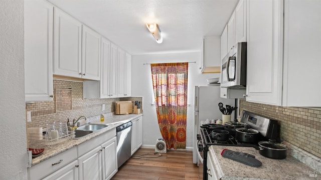 kitchen featuring sink, light hardwood / wood-style flooring, light stone countertops, white cabinetry, and stainless steel appliances