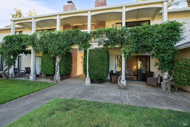 entrance to property featuring a patio area, brick siding, a chimney, and a lawn