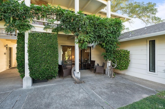 view of exterior entry with roof with shingles and a patio