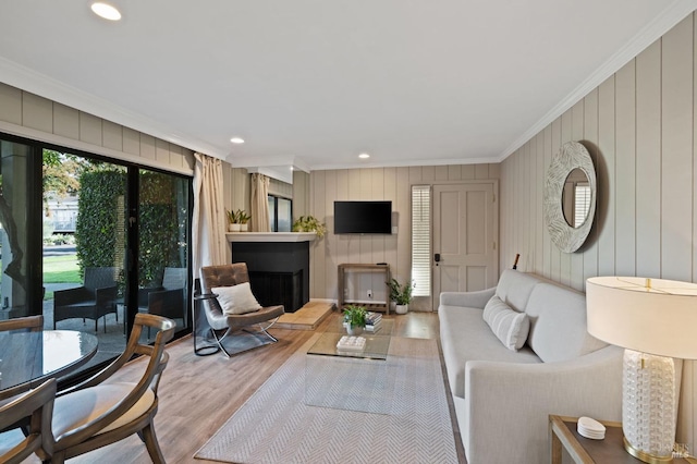 living room featuring a fireplace with raised hearth, recessed lighting, wood finished floors, and crown molding