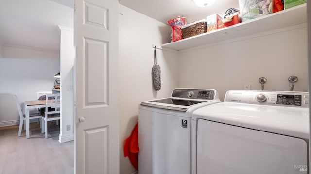 clothes washing area featuring laundry area, light wood-style flooring, washing machine and dryer, and baseboards